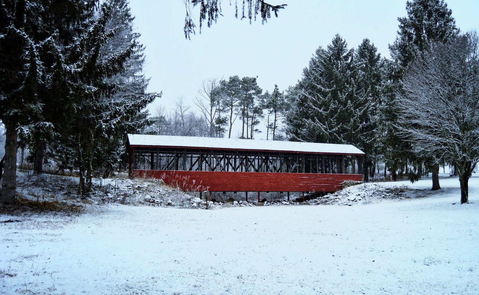 A beautiful winter scene featuring a red covered bridge surrounded by snow-blanketed trees.