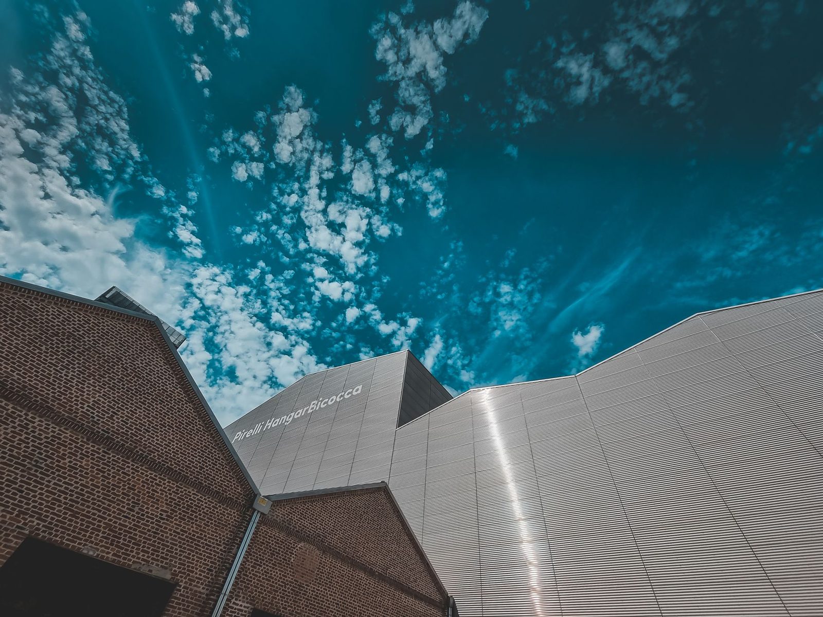Dramatic low-angle view of modern building facade under a cloudy blue sky, showcasing architectural beauty.