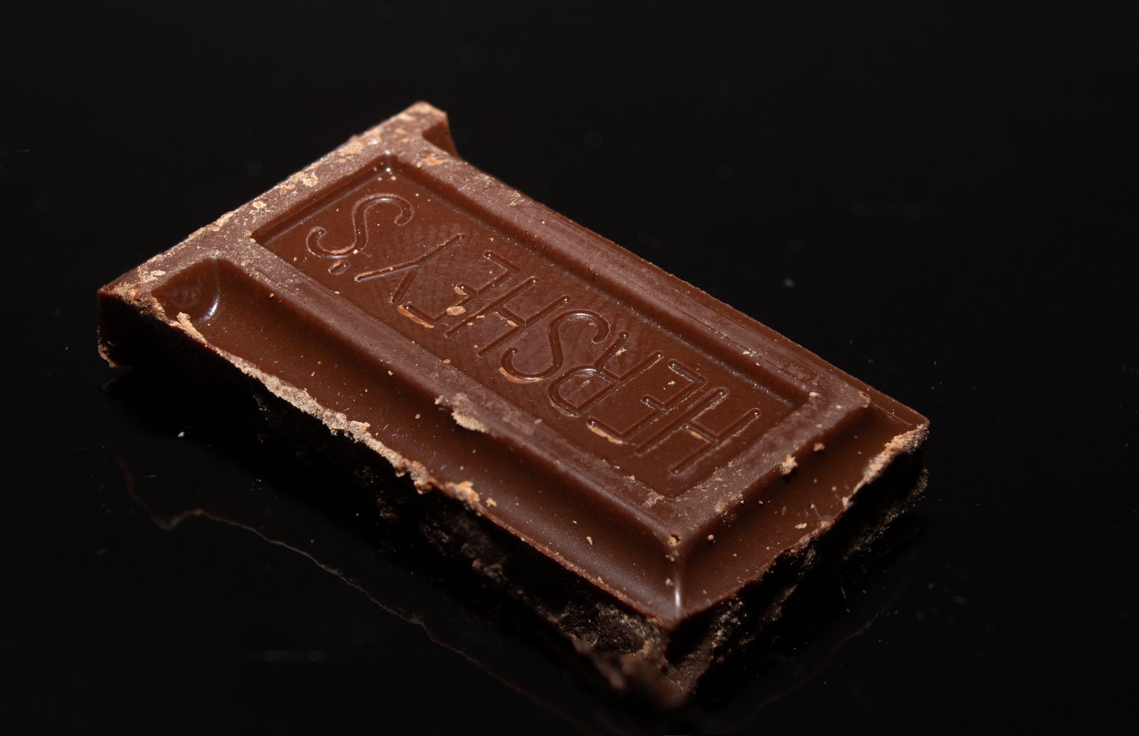 Macro shot of a Hershey's chocolate piece on a shiny black background.