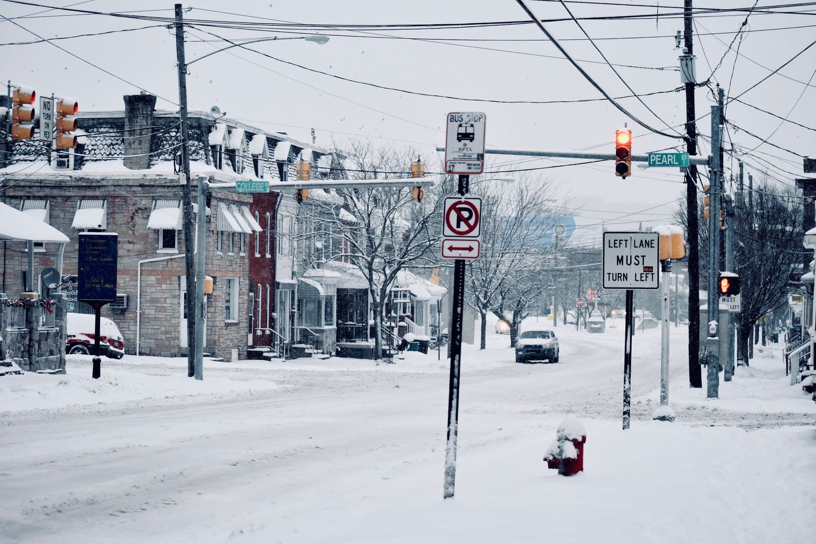 A winter street view in Lancaster, PA showcasing snowy roads, traffic signs, and parked vehicles.