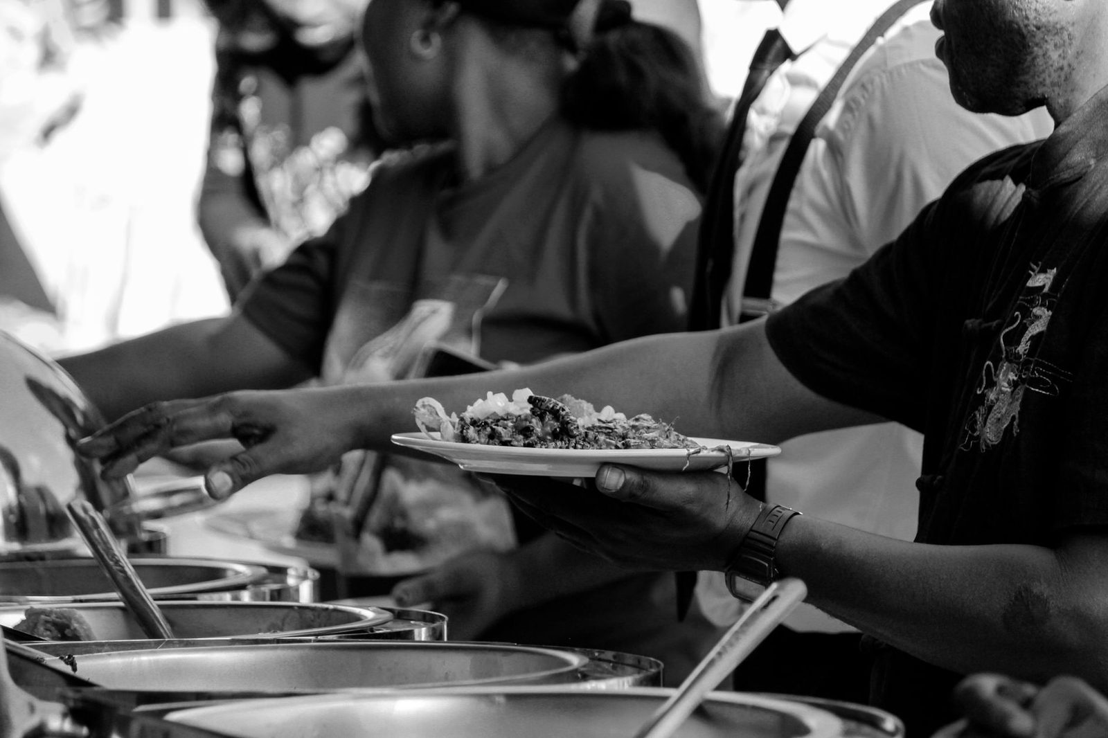 Black and white of crop anonymous group of people serving food in plates while visiting smorgasbord