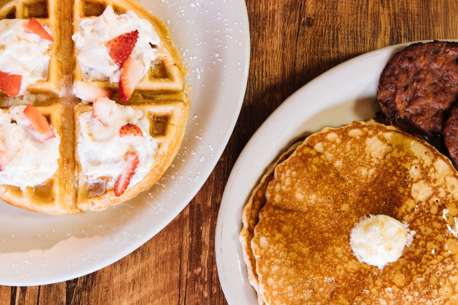 Enjoy a classic American breakfast featuring pancakes, waffles, and sausages topped with whipped cream and strawberries.
