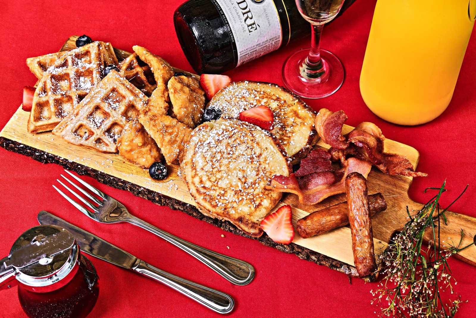 A vibrant breakfast setup with pancakes, waffles, bacon, and fresh fruit on a wooden tray.