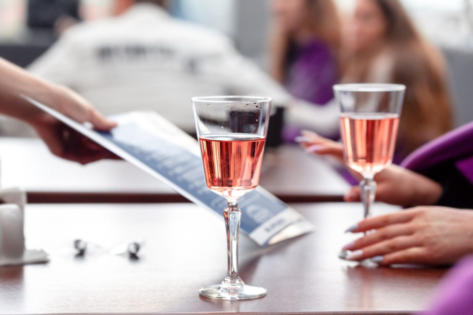 Two elegant glasses of rosé wine on a table in a social setting with blurred background.
